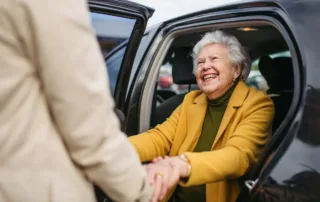 A senior woman being helped out of her car, happy and enjoying retirement stress-free after their child answered the question, How do I monitor my elderly parents’ finances?