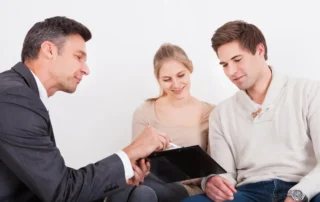 Advisor meets young couple, explaining 3 considerations before choosing a private fiduciary indoors.