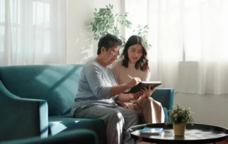Older woman and younger advisor review trustee documents on a tablet while seated on a sofa at home.