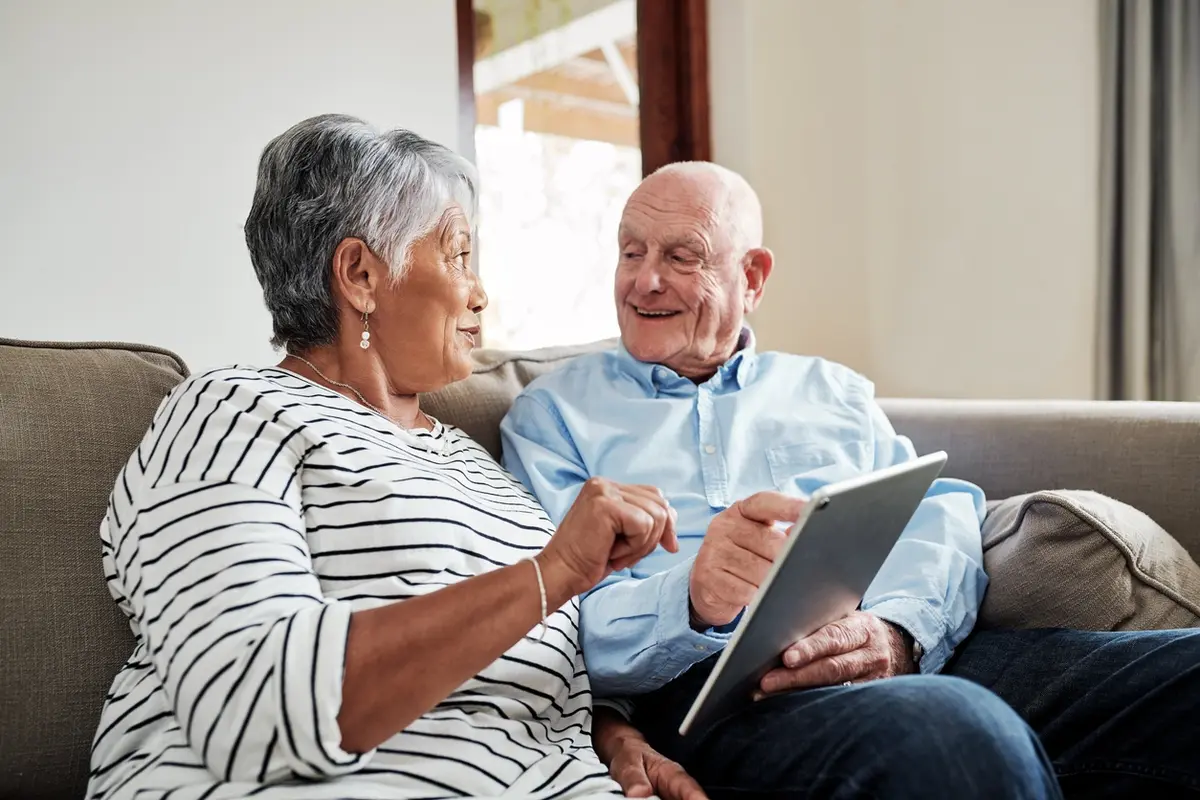 Senior couple reviews tablet while discussing Transitioning Your Elderly Parents’ Finances together.