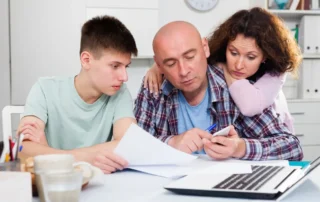 Family reviews trustee paperwork and finances together at home table with laptop and documents open