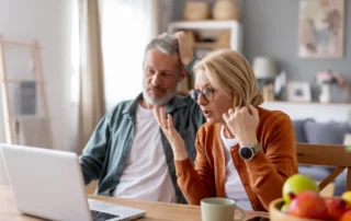 Older couple looks worried at laptop while learning how to avoid scams targeting seniors at home
