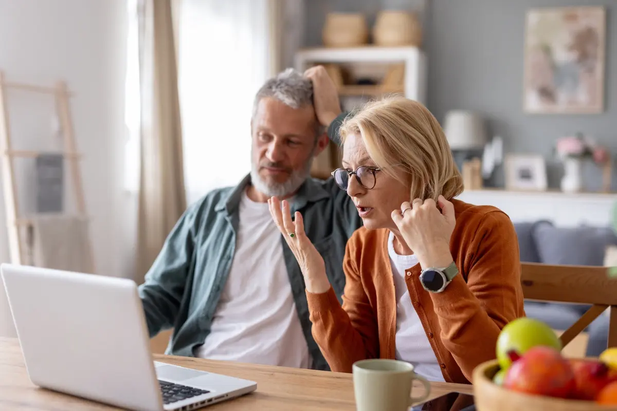 Older couple looks worried at laptop while learning how to avoid scams targeting seniors at home