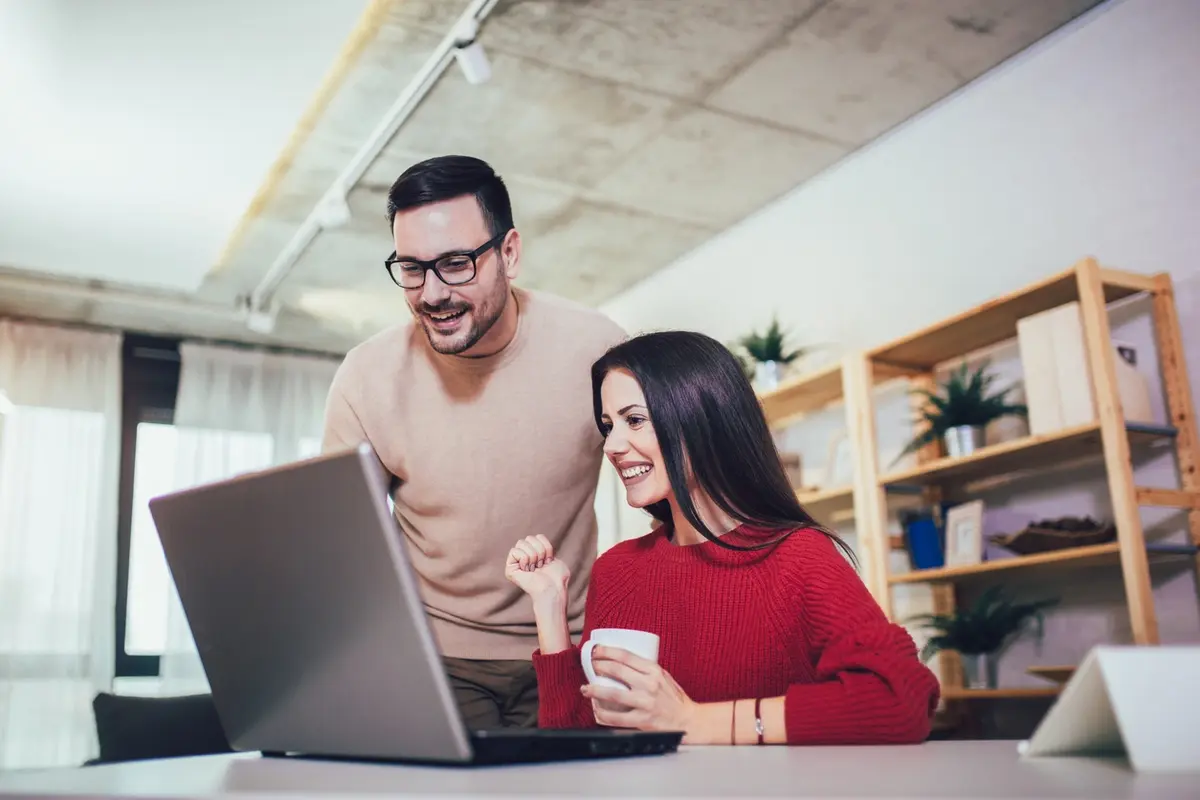 Couple smiles at laptop, planning ahead for how to make next year’s tax season more successful
