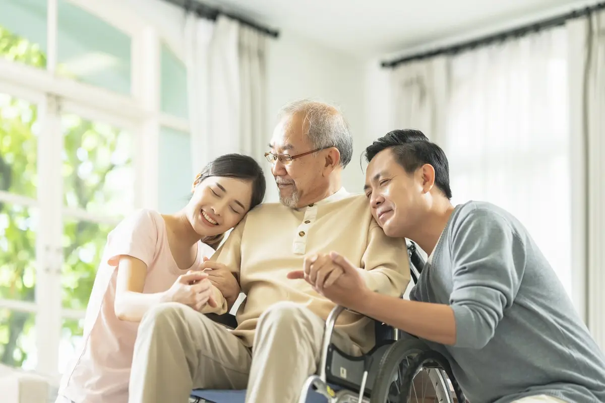 How To Share Caregiving Responsibilities For An Aging Parent Adult son and daughter comfort father in wheelchair, sharing caregiving responsibilities