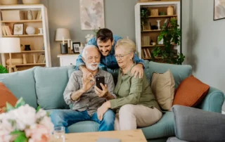 Adult son helps older parents review a smartphone, showing how to decrease your parents financial decisions with age