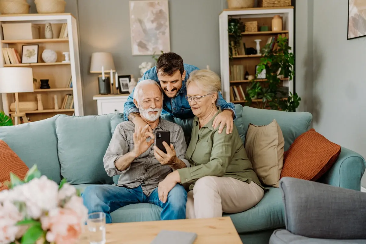 Adult son helps older parents review a smartphone, showing how to decrease your parents financial decisions with age