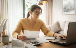 Woman reviews bills and laptop at home while filing the final tax return after someone dies