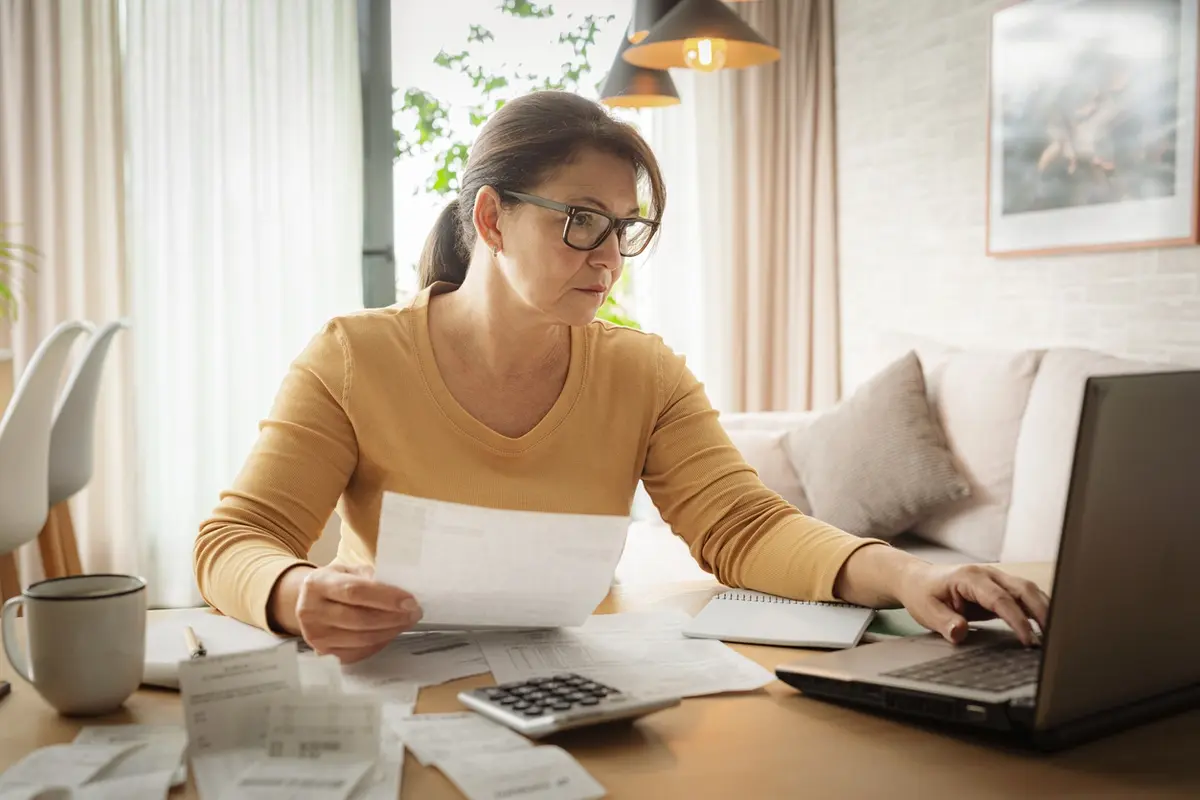Woman reviews bills and laptop at home while filing the final tax return after someone dies