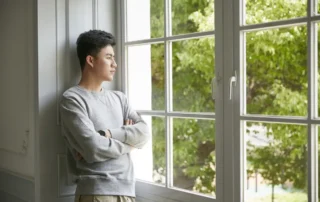 Young man reflects on Probate concerns while standing by a window at home