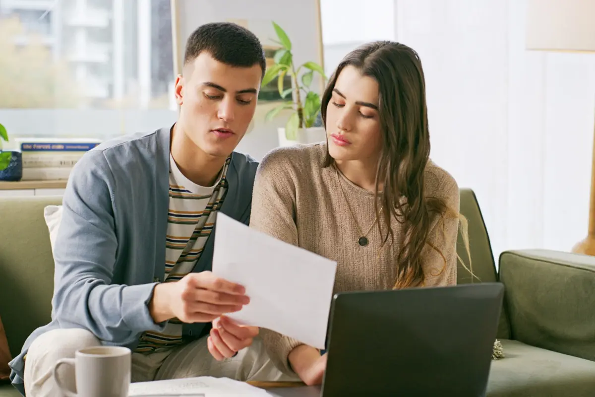 Tax Scams to Watch Out For Post Tax Season: couple reviews paperwork and laptop at home