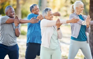 Four seniors stretch outdoors together, showing the benefits of daily exercise for seniors