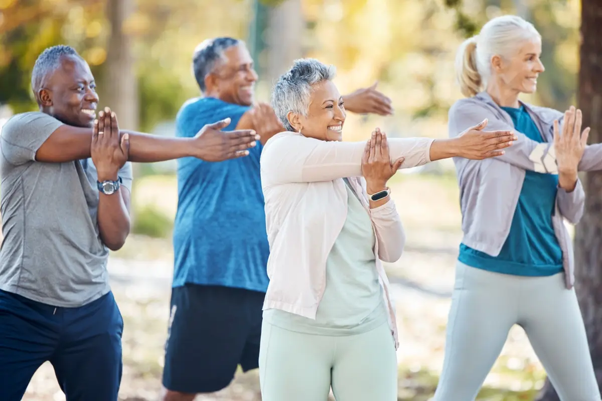 Four seniors stretch outdoors together, showing the benefits of daily exercise for seniors