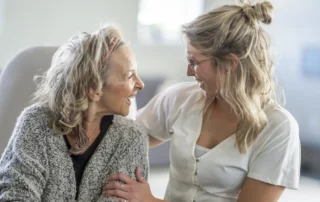 Daughter hugs older mother at home, showing loving support for aging parent care and daily comfort