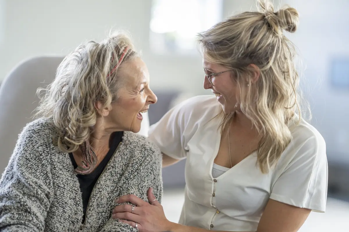 Daughter hugs older mother at home, showing loving support for aging parent care and daily comfort
