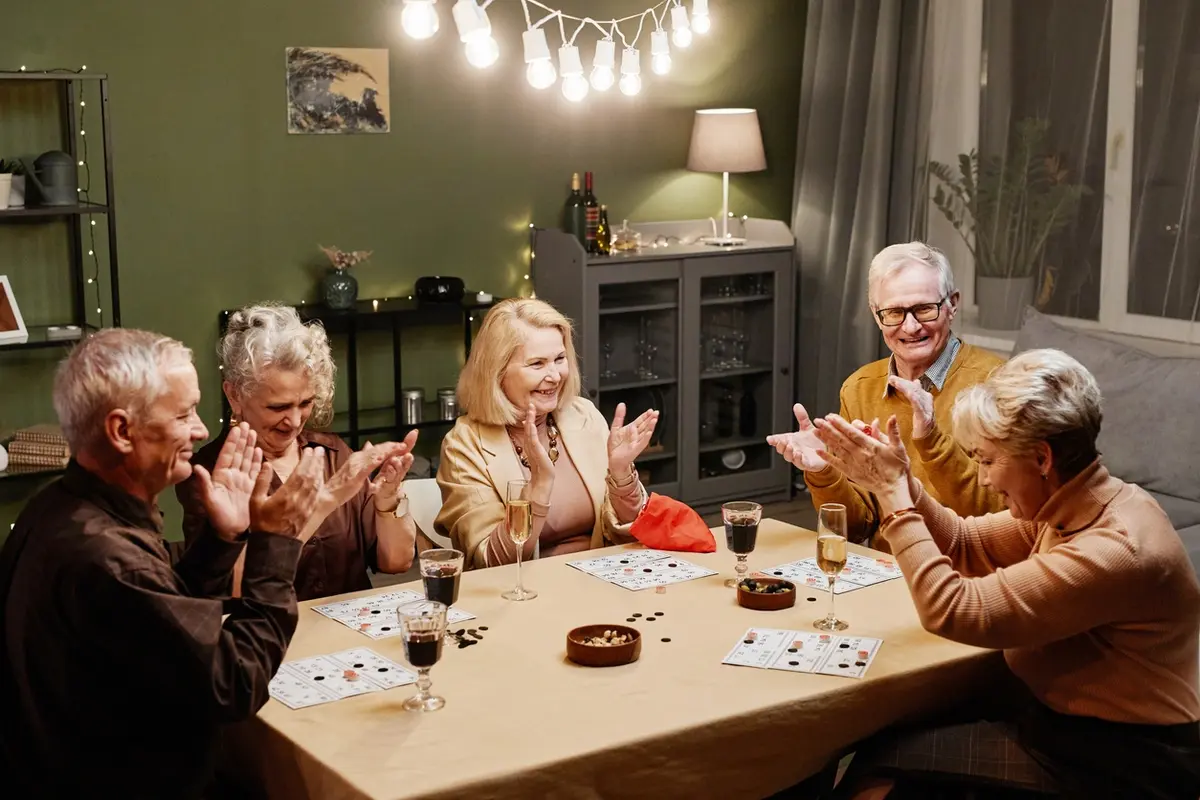 Seniors clap and smile around a table, enjoying top holiday activities for seniors this year