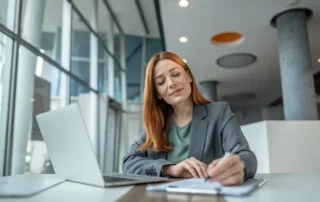 Professional writes notes beside laptop for Trust Accounting Basics and Tips for New Trustees guide.
