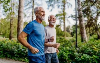 Two older men jog through a park, illustrating ways for seniors to stay healthy and active