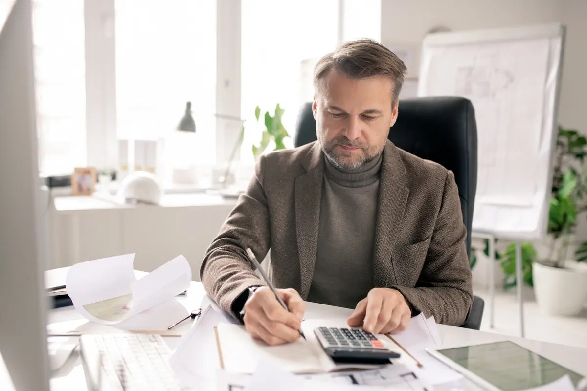 Man works through tax paperwork with calculator at desk, illustrating the 2021 Tax Deadline guide