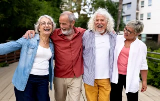 Four older friends walk arm in arm outdoors, smiling as they plan retirement at 65 or 85