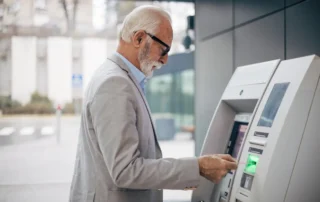 Elderly man withdrawing money from an ATM with a debit card, showing a financial moment connected to elder financial exploitation concerns.