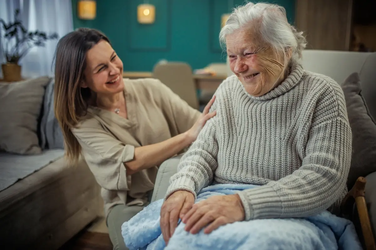Hiring a Caregiver for Elderly Parent Home Support Cheerful mature woman embracing her senior mother at home while considering hiring a caregiver for elderly parent support.