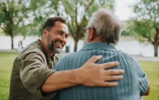 Adult son comforting his elderly parent outdoors, representing expenses that occur after a parent dies.