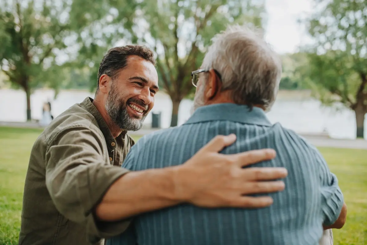 Adult son comforting his elderly parent outdoors, representing expenses that occur after a parent dies.